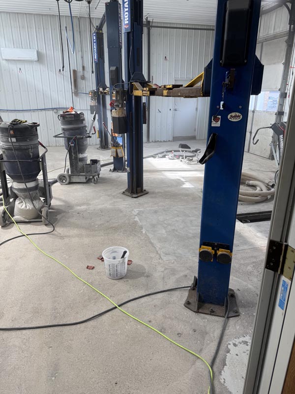 Auto shop floor before — bare concrete mid-grind with dust vacuums and car lifts