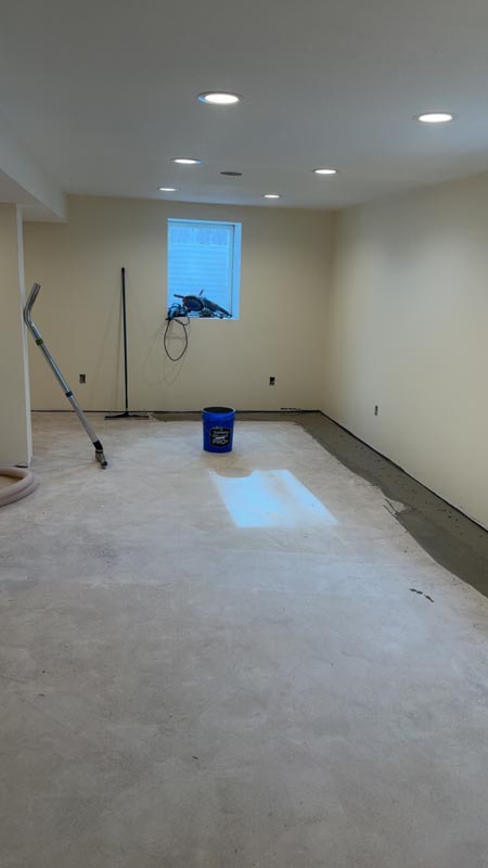 Basement floor before - bare prepped concrete with recessed lighting and prep tools