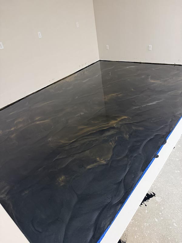 Black and gold metallic epoxy floor being installed, wet glossy swirl pattern with blue tape