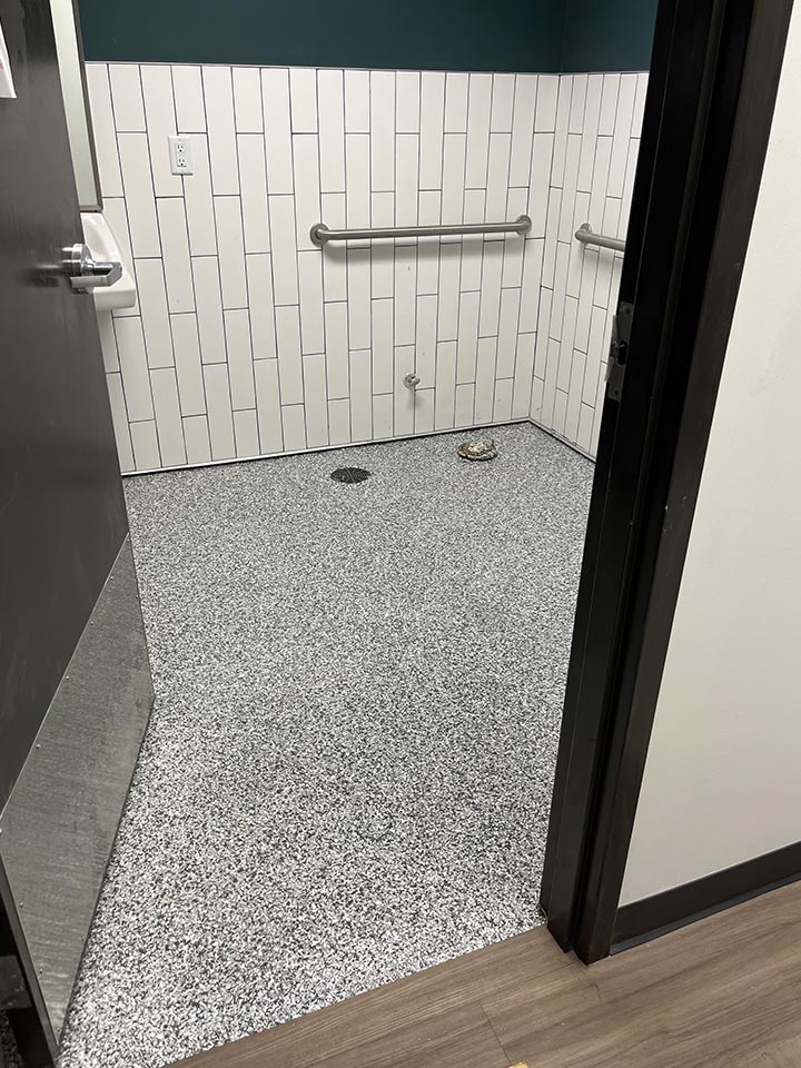 Chemical-resistant flake floor with coved base in a commercial restroom, ADA compliant