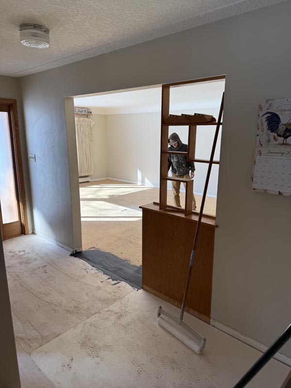Residential entry before - bare floor mid-prep with masked worker and roller