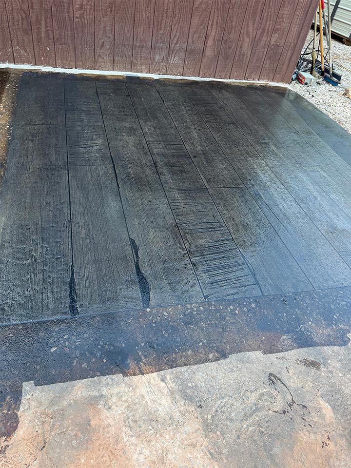 Outdoor stamped concrete in a wood-plank pattern with dark wet stain