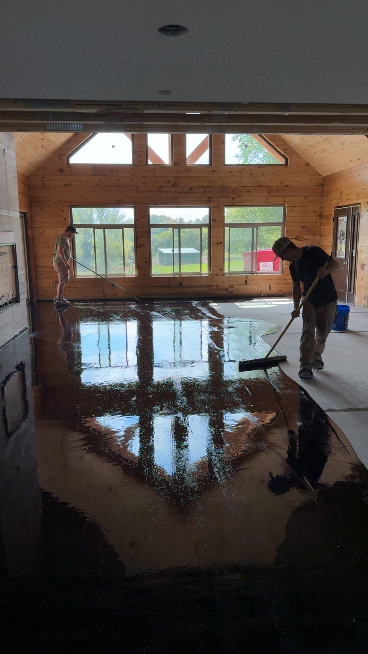 Crew spreading dark wet stain/flood coat in a timber-frame great room
